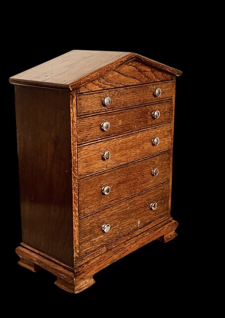 An English Antique Apprentice Piece Chest of Drawers having a pediment top above five graduated drawers.