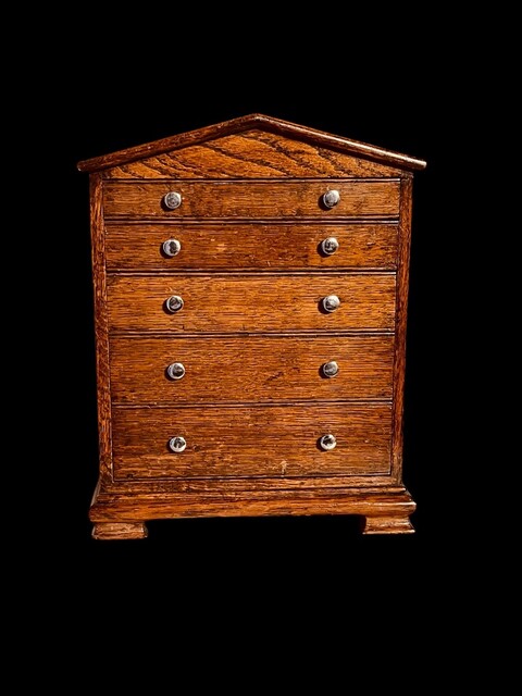 An English Antique Apprentice Piece Chest of Drawers having a pediment top above five graduated drawers.